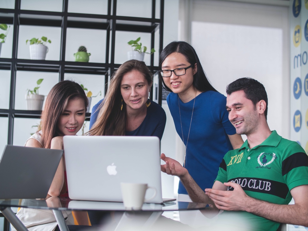 four people sitting around a table looking at laptop